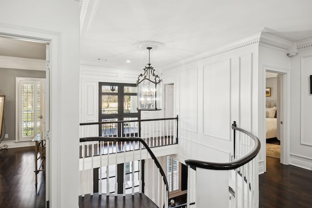 staircase with hardwood / wood-style flooring, a notable chandelier, plenty of natural light, and ornamental molding