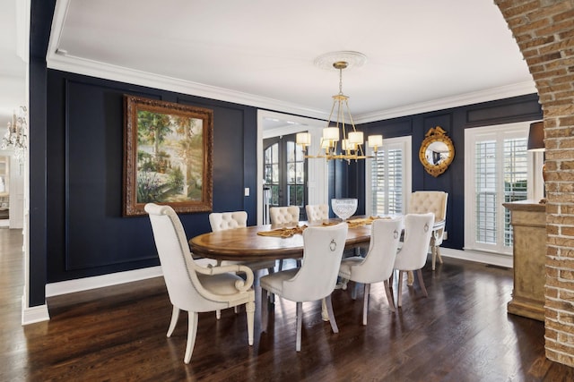 dining area featuring crown molding, baseboards, wood finished floors, a notable chandelier, and a decorative wall