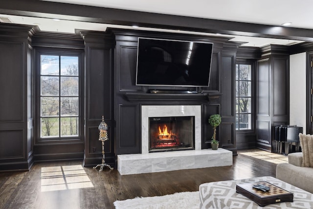 living room with beam ceiling, a decorative wall, crown molding, and wood finished floors