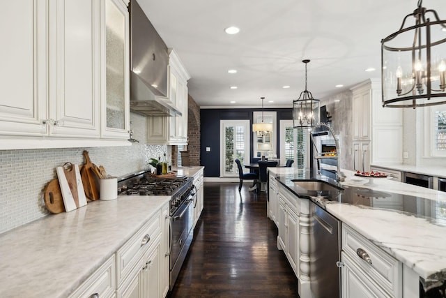 kitchen featuring a notable chandelier, tasteful backsplash, white cabinetry, stainless steel appliances, and wall chimney range hood