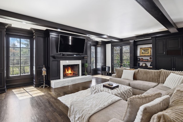 living room featuring wood finished floors, beamed ceiling, a decorative wall, and a healthy amount of sunlight