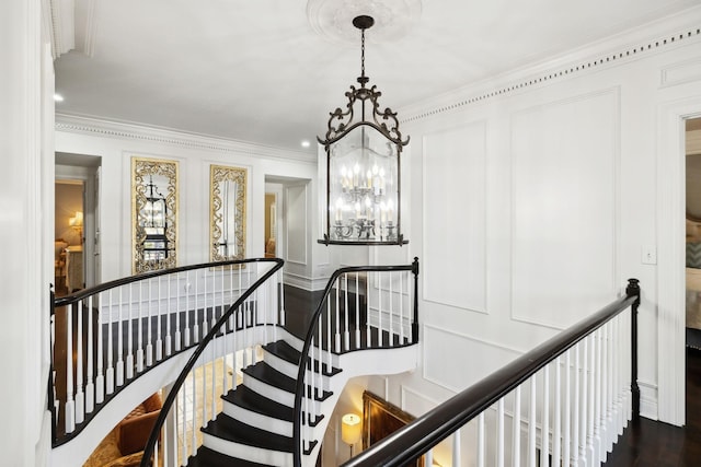 stairs featuring a decorative wall, a notable chandelier, wood finished floors, and ornamental molding