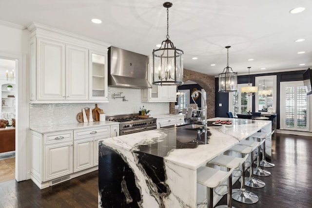 kitchen with a sink, double oven range, arched walkways, wall chimney exhaust hood, and a chandelier