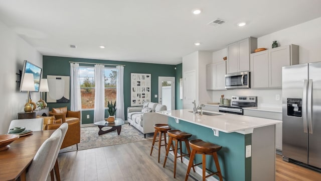 kitchen with light wood-type flooring, a breakfast bar, stainless steel appliances, a kitchen island with sink, and sink