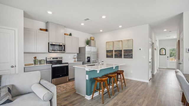 kitchen featuring gray cabinetry, an island with sink, appliances with stainless steel finishes, light hardwood / wood-style floors, and a breakfast bar area