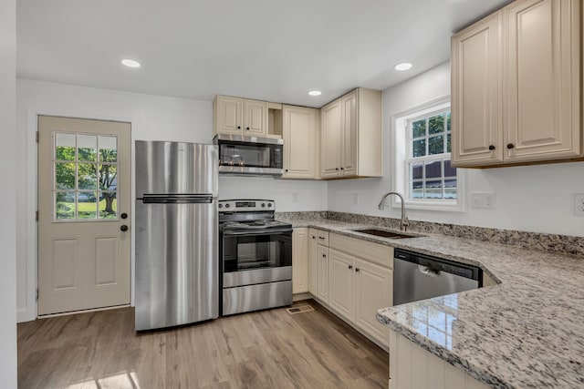 kitchen with appliances with stainless steel finishes, light stone counters, a healthy amount of sunlight, and sink