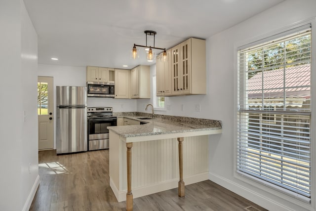 kitchen featuring sink, hanging light fixtures, stainless steel appliances, light hardwood / wood-style flooring, and kitchen peninsula