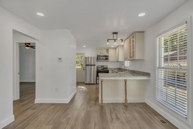 kitchen featuring kitchen peninsula, appliances with stainless steel finishes, decorative light fixtures, and light hardwood / wood-style floors