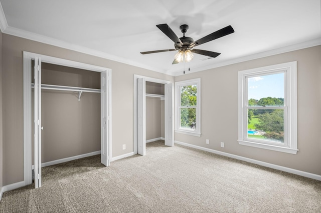 unfurnished bedroom featuring ceiling fan, light colored carpet, crown molding, and two closets