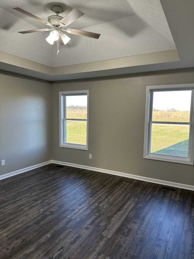 empty room featuring a textured ceiling, a raised ceiling, ceiling fan, and dark wood-type flooring