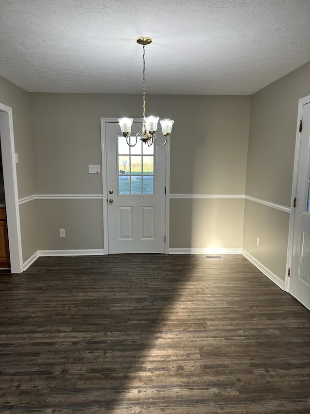 entrance foyer featuring dark wood-type flooring, a textured ceiling, and a notable chandelier