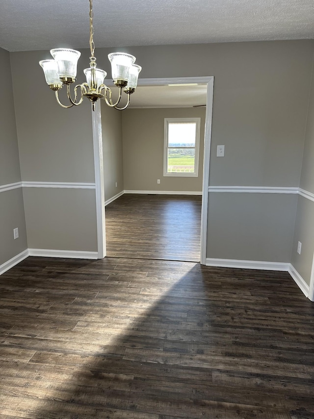 empty room featuring a textured ceiling, a chandelier, and dark hardwood / wood-style floors