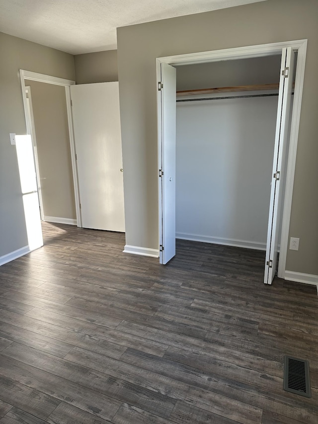 unfurnished bedroom with dark hardwood / wood-style floors, a textured ceiling, and a closet