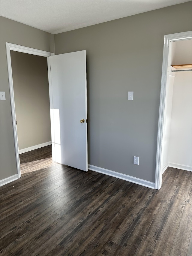 unfurnished bedroom featuring a spacious closet, dark wood-type flooring, and a closet