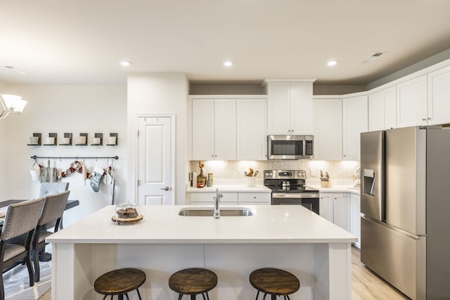 kitchen featuring white cabinetry, sink, light hardwood / wood-style flooring, a center island with sink, and appliances with stainless steel finishes