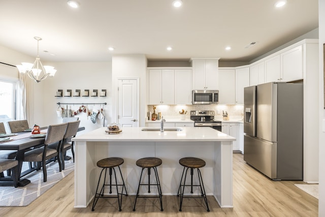 kitchen with appliances with stainless steel finishes, light hardwood / wood-style floors, white cabinetry, and a kitchen island with sink