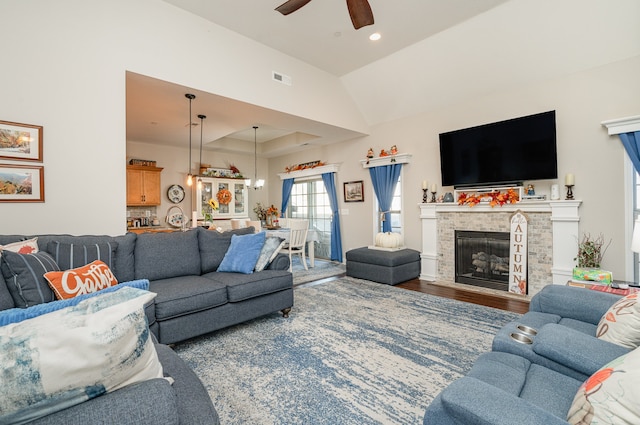 living room with wood-type flooring, vaulted ceiling, ceiling fan, and a stone fireplace