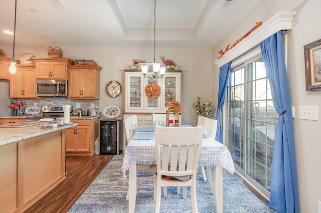 dining room featuring a chandelier, dark hardwood / wood-style flooring, a raised ceiling, and beverage cooler