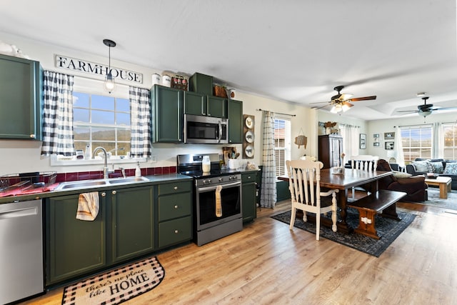 kitchen featuring sink, green cabinets, decorative light fixtures, appliances with stainless steel finishes, and light wood-type flooring