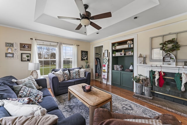 living room with a raised ceiling, ceiling fan, and dark wood-type flooring