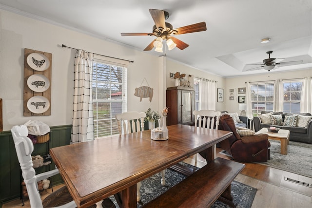 dining room featuring wood-type flooring, a raised ceiling, ceiling fan, and crown molding