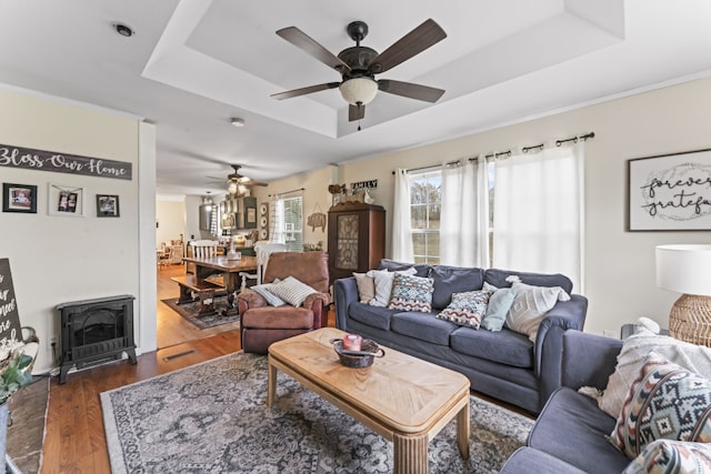 living room featuring a raised ceiling, a wood stove, ceiling fan, and dark hardwood / wood-style flooring