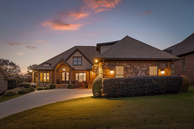 view of front of home featuring a lawn, stone siding, driveway, and a shingled roof