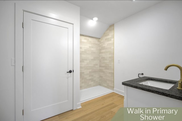 bathroom featuring vanity, a tile shower, wood-type flooring, and vaulted ceiling