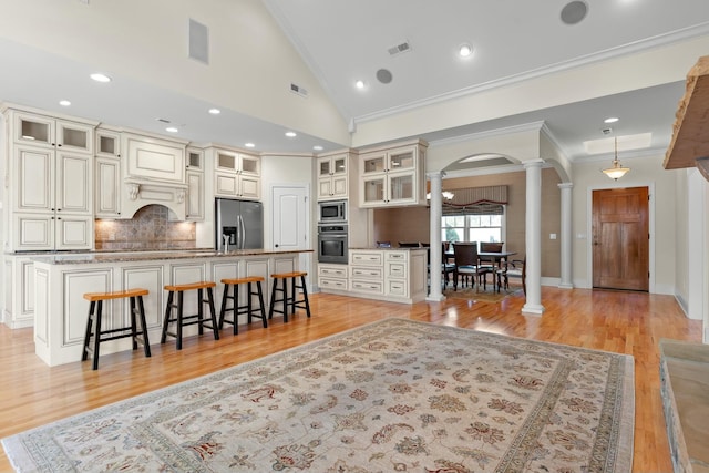 kitchen featuring ornate columns, a large island, stainless steel appliances, a kitchen breakfast bar, and light wood-type flooring