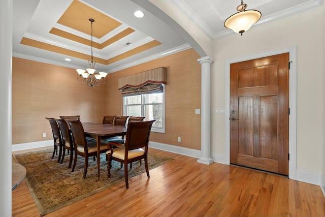 dining area with a raised ceiling, a chandelier, light wood-type flooring, ornamental molding, and decorative columns