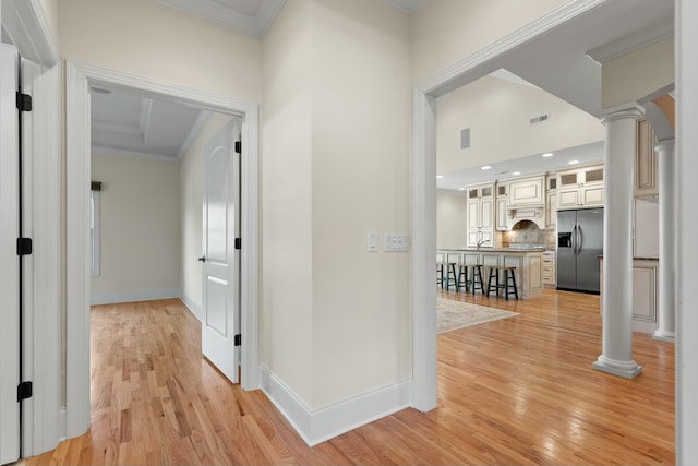 hallway featuring light hardwood / wood-style flooring, ornate columns, crown molding, and sink