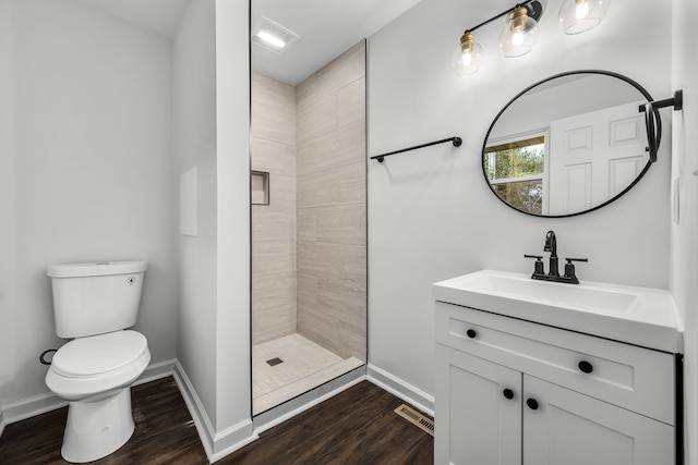 bathroom with toilet, a tile shower, wood-type flooring, and vanity