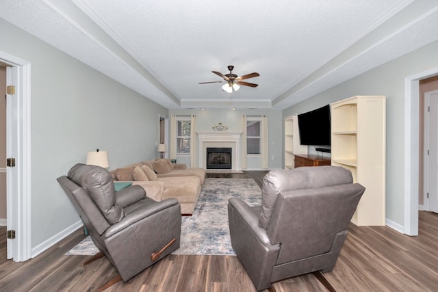 living room with a textured ceiling, dark hardwood / wood-style flooring, a tray ceiling, and ceiling fan