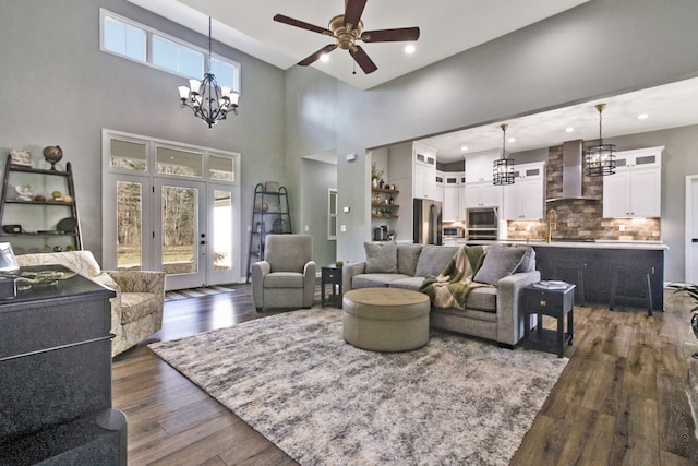 living room with plenty of natural light, dark hardwood / wood-style flooring, a towering ceiling, and ceiling fan with notable chandelier