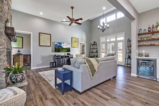 living room featuring ceiling fan with notable chandelier, beverage cooler, a high ceiling, and wood-type flooring