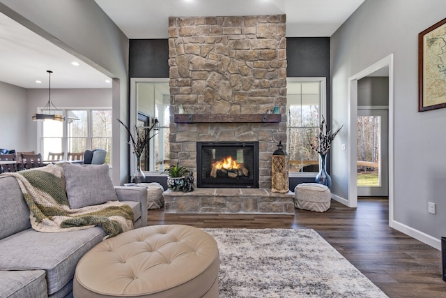 living room featuring a stone fireplace and dark wood-type flooring