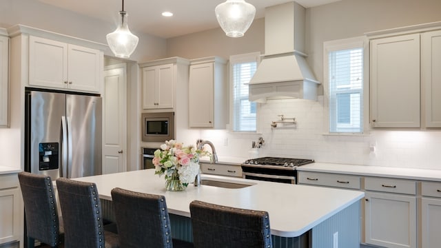 kitchen featuring decorative light fixtures, stainless steel appliances, a kitchen island with sink, and custom exhaust hood