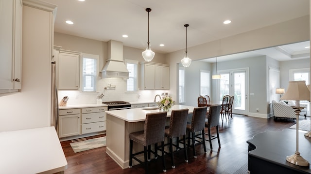 kitchen featuring custom exhaust hood, decorative light fixtures, dark wood-type flooring, and a kitchen island with sink