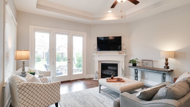 living room with hardwood / wood-style flooring, ceiling fan, and a tray ceiling