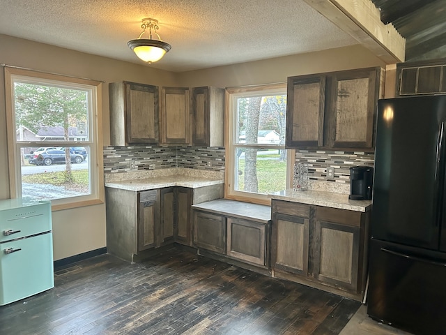 kitchen featuring decorative backsplash, dark hardwood / wood-style floors, black fridge, and a wealth of natural light