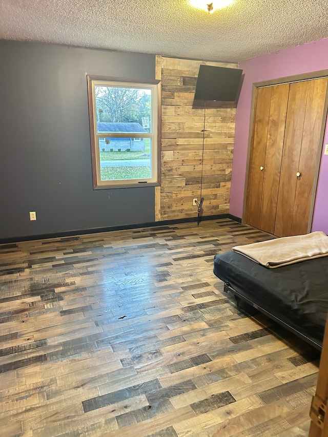 bedroom featuring wooden walls, a closet, wood-type flooring, and a textured ceiling