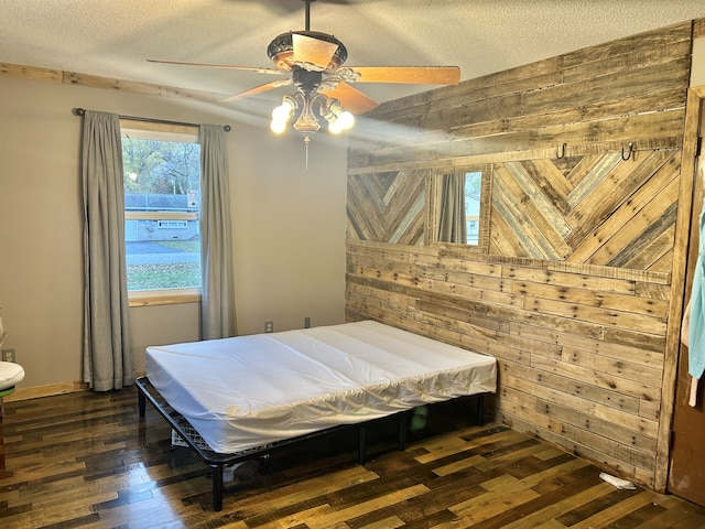 bedroom featuring a textured ceiling, ceiling fan, wooden walls, and dark hardwood / wood-style floors