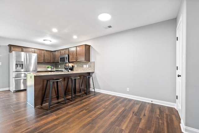 kitchen featuring backsplash, dark hardwood / wood-style floors, appliances with stainless steel finishes, a kitchen bar, and kitchen peninsula