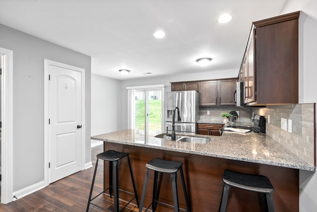 kitchen with light stone counters, dark hardwood / wood-style flooring, kitchen peninsula, a breakfast bar, and appliances with stainless steel finishes