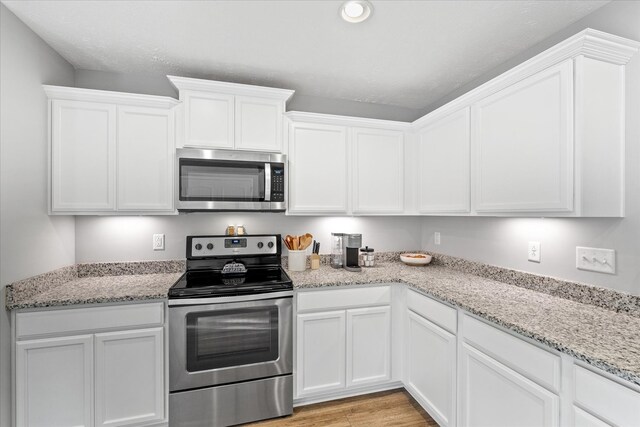 kitchen with light stone counters, stainless steel appliances, light hardwood / wood-style floors, and white cabinets