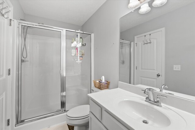 bathroom with a textured ceiling, walk in shower, vanity, and toilet