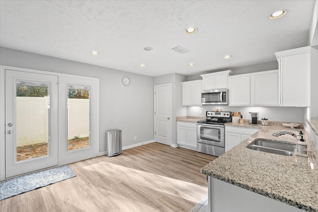 kitchen featuring appliances with stainless steel finishes, white cabinetry, light stone countertops, and sink