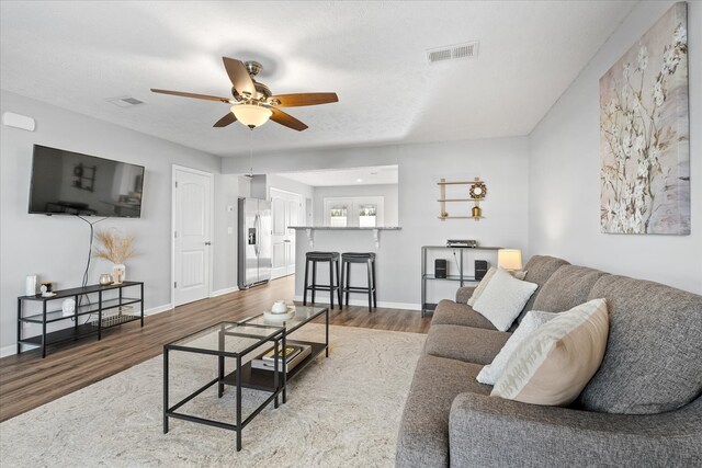 living room featuring wood-type flooring, a textured ceiling, and ceiling fan