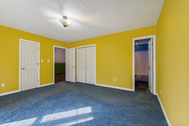 unfurnished bedroom with ensuite bath, dark carpet, and a textured ceiling