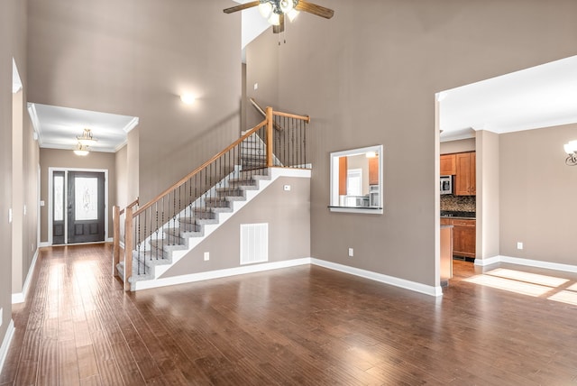 unfurnished living room featuring hardwood / wood-style floors, ceiling fan with notable chandelier, ornamental molding, and a towering ceiling